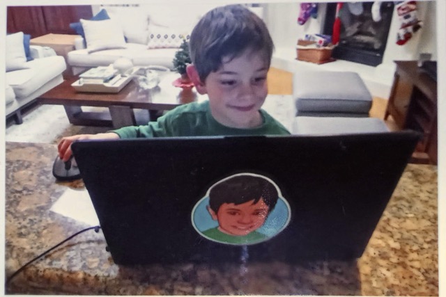 elliot as a child sitting in front of his first laptop computer smiling