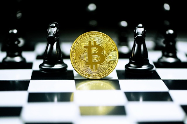 Gold bitcoin surrounded by chess peices on a chess board